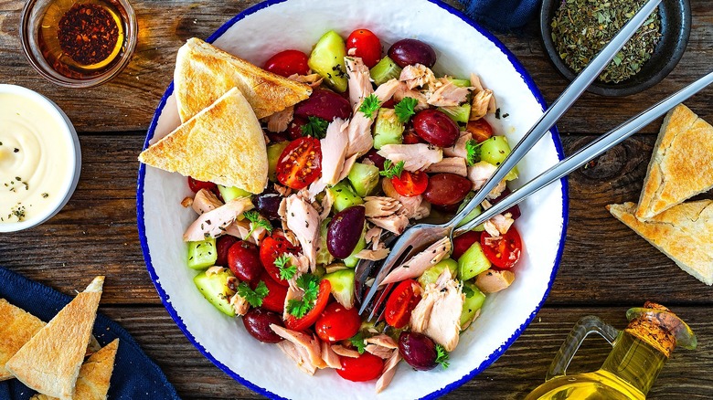 Top-down view of tuna salad with kalamata olives, cucumbers, and cherry tomatoes in a white bowl with blue trim