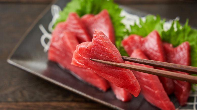 Tuna sashimi held by chopsticks over a plate
