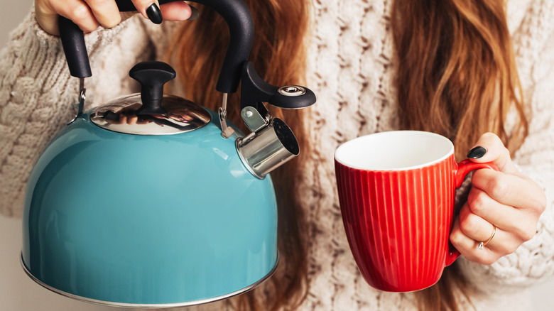Person holding a kettle and a coffee mug