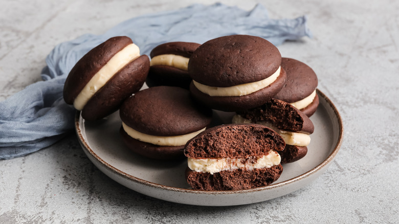 A plate of whoopie pies with one that is broken in half.