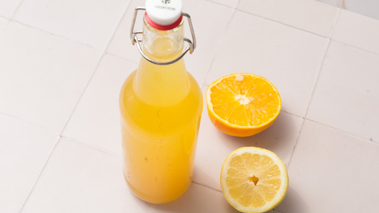 A bottle of citrus flavored vodka near two citrus halves