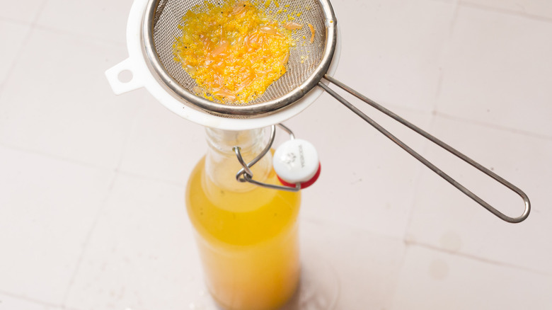 Straining citrus through sieve into bottle