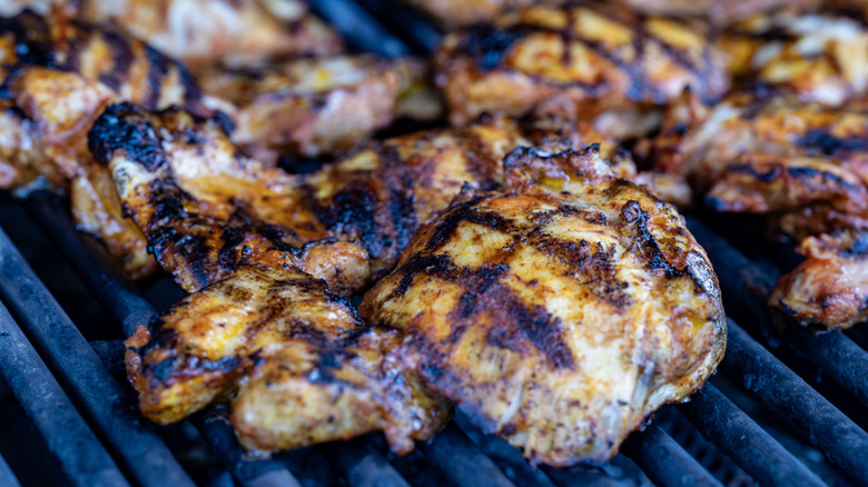 Marinated chicken thighs cooking on the grill, covered in criss-crossed grill marks.
