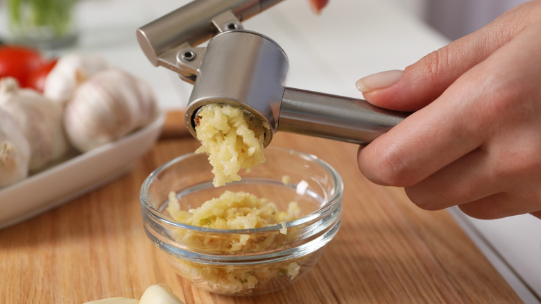 Hands squeeze garlic through garlic press