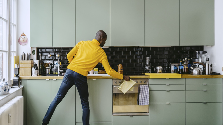 man cooking in front of sage green kitchen cabinets