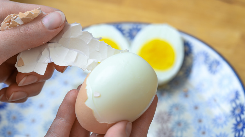 Woman's hand peeling a hard-boiled egg.