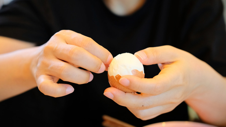 Hands peeling a hard-boiled egg.