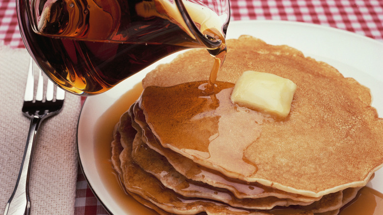 syrup pitcher pouring syrup onto stack of pancakes