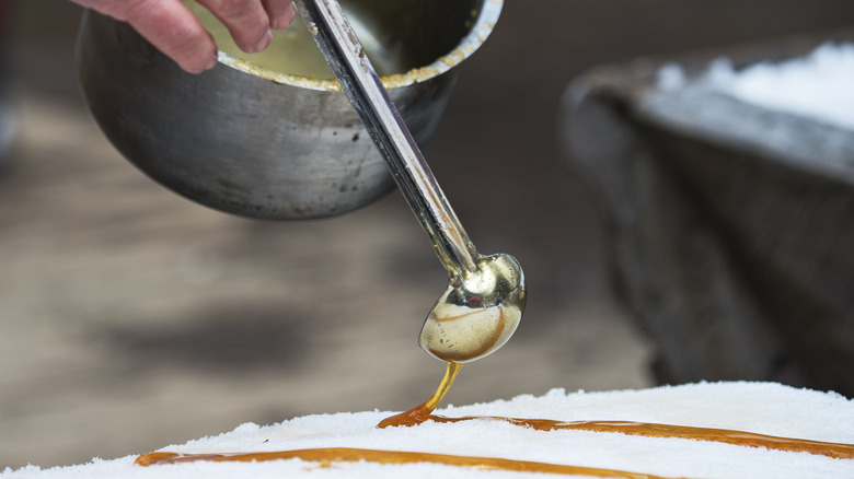 hand pouring boiled maple syrup onto fresh snow
