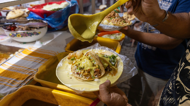 person ladling sauce on a taco at a taco stand in Mexico