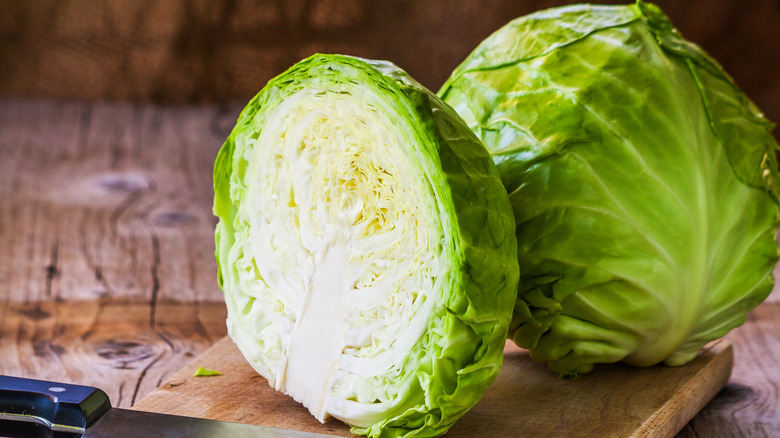 A whole head of cabbage and a half a head of cabbage sitting on a cutting board with a knife