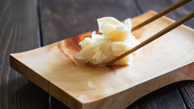 Pickled ginger being picked up by two chopsticks.