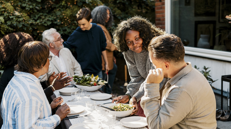 a woman offering food to a guest at an outdoor dinner party