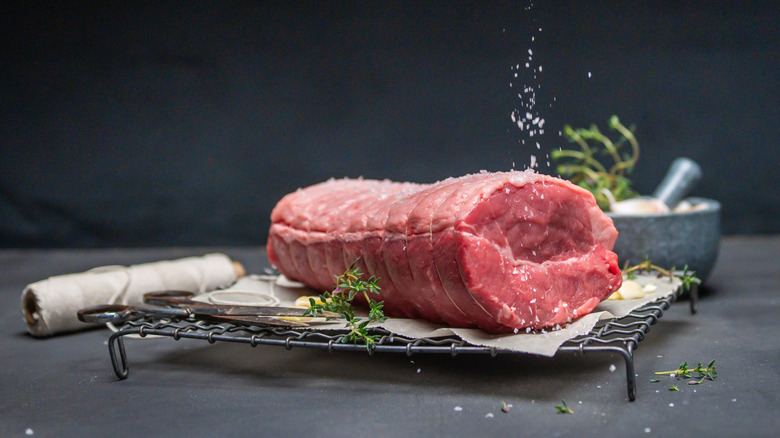 A trussed beef tenderloin being seasoned from above