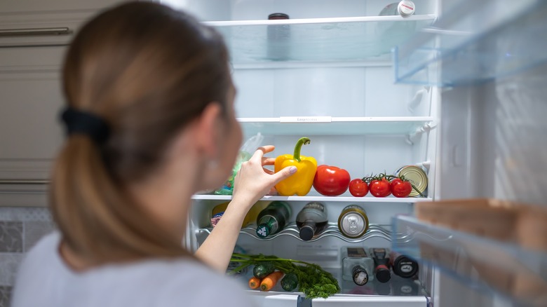 A woman taking a bell pepper out of a refrigerator.
