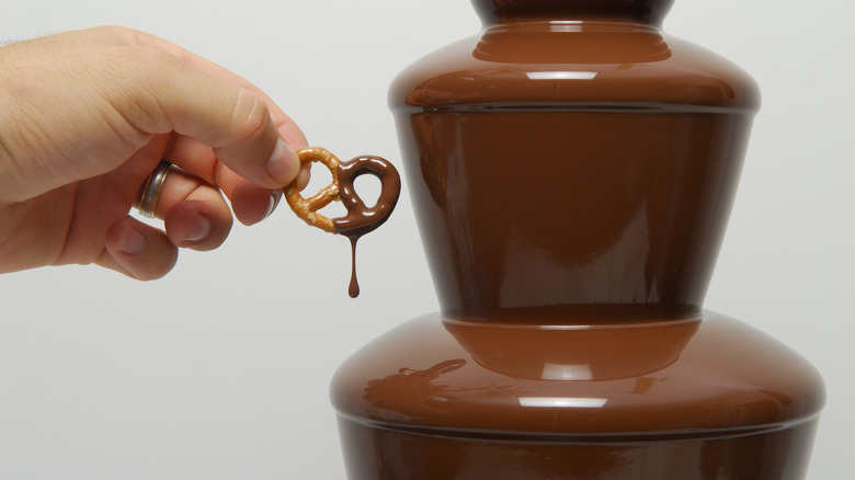 Hand putting pretzel in chocolate fondue
