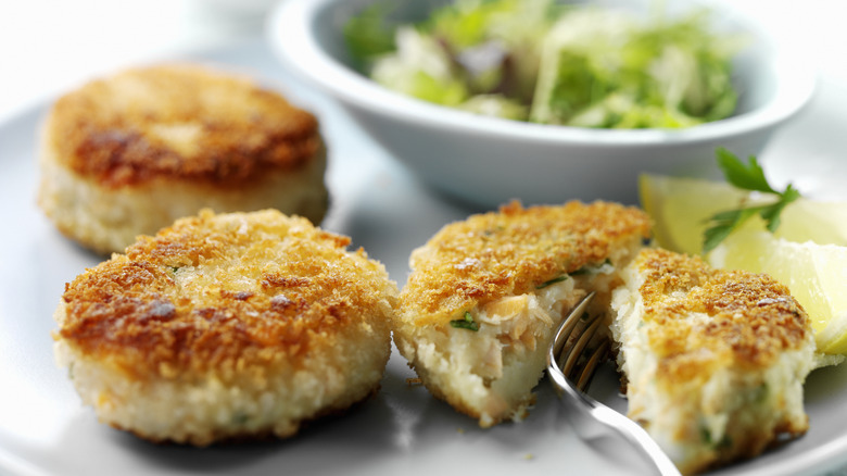 Three crab cakes on a plate, one of which has been cut in half .