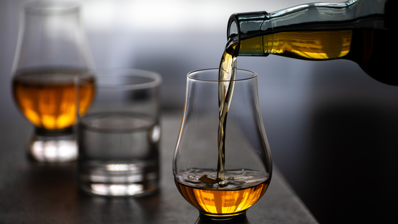 Scotch being poured into glass next to water on countertop.