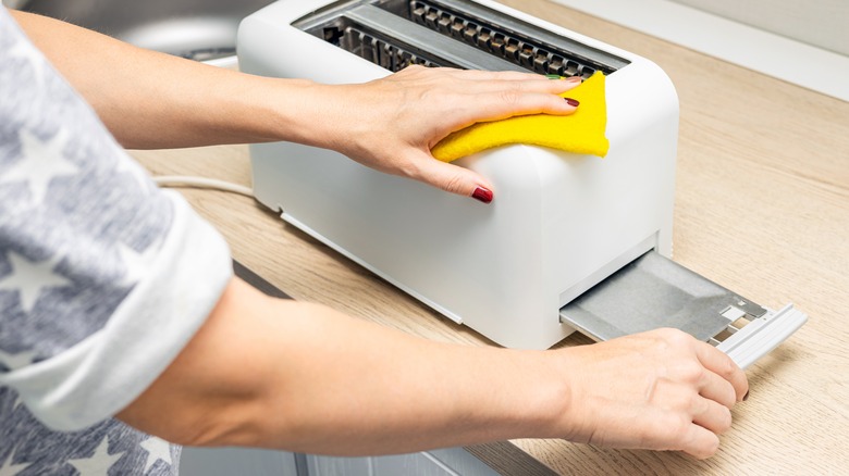 Hand wiping the outside of a toaster with a small cloth