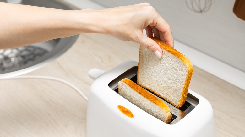 woman's hand loading bread into a toaster