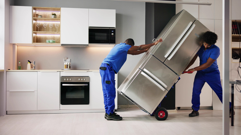Two people moving a fridge in a kitchen