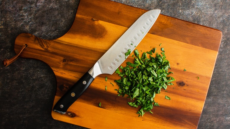 Overhead shot of a chefs knife on a cutting board with chopped parsley