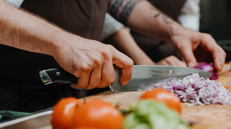 Close up of a chef using proper pinch grip while chopping a red onion