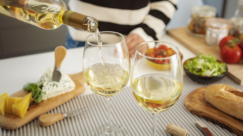 A woman pours white wine into two glasses