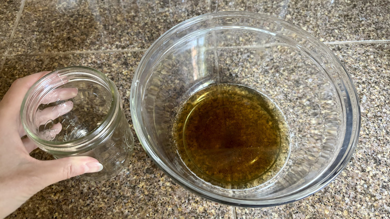 A hand placing a Ball jar next to a bowl of bacon grease