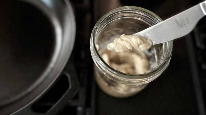 A knife scooping bacon grease out of a jar
