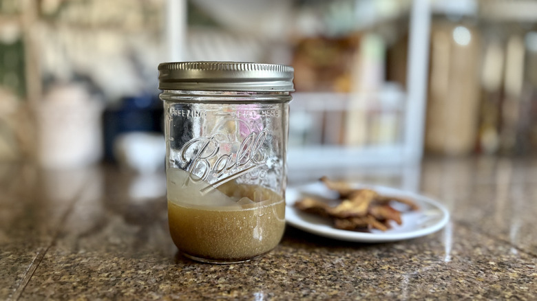 A jar of bacon grease with the lid on next to a plate of crispy bacon on a kitchen counter