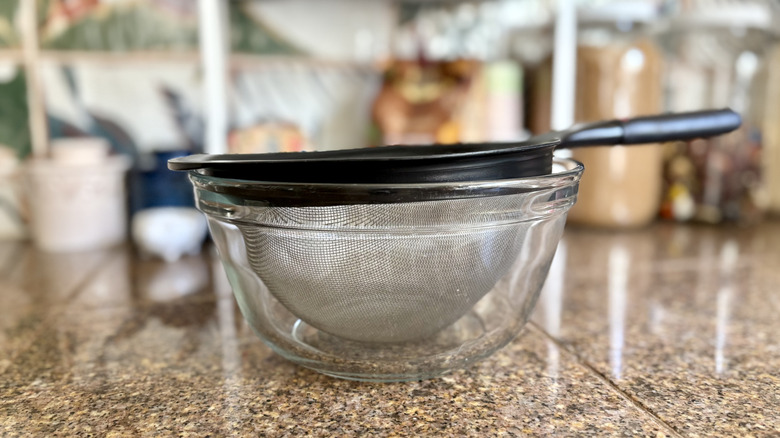 A strainer sitting inside a glass bowl on a kitchen counter