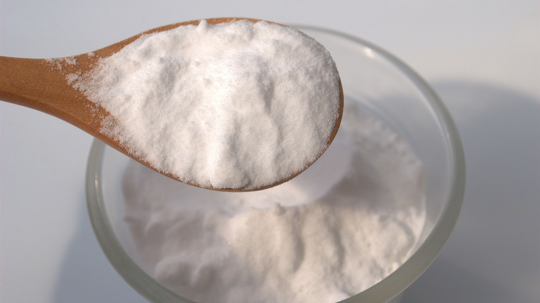 A spoon filled with baking soda over a bowl of baking soda