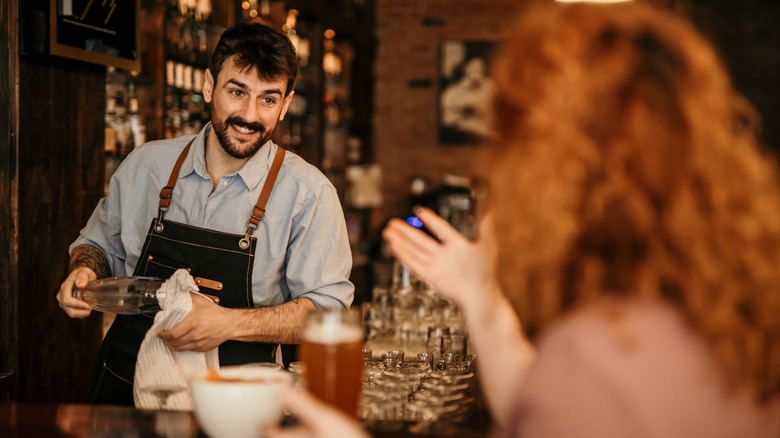 bartender dries glass while redheaded customer talks