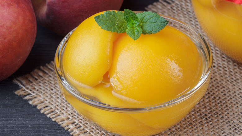 Blemish-free peeled peaches in a glass bowl with a sprig of mint