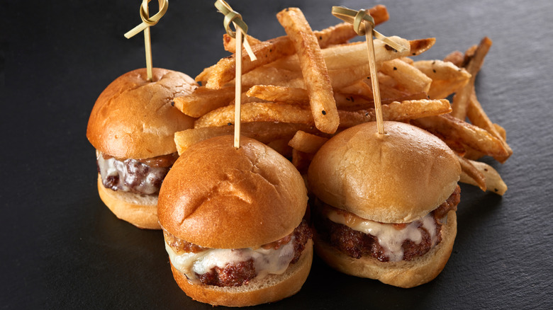 Three burger sliders with toothpicks in front of fries.