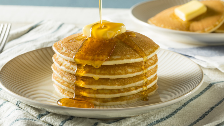 stack of pancakes with butter and maple syrup being poured on top