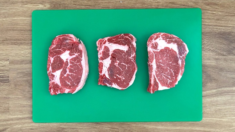 Three uncooked ribeye steaks on a green cutting board