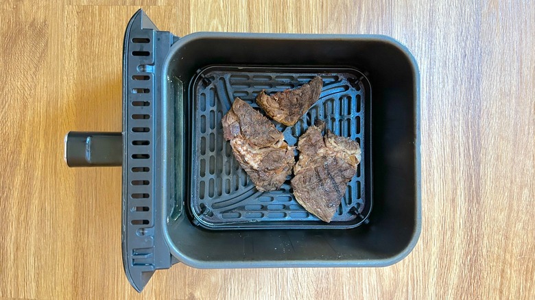Air fryer basket with pieces of ribeye steak in it