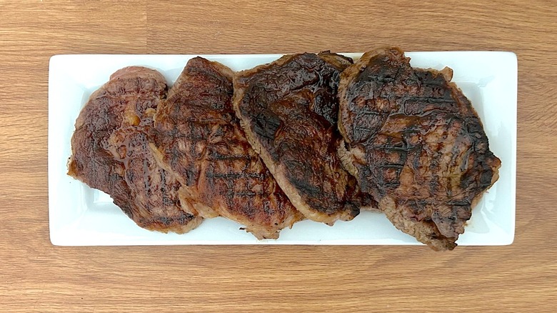 Four grilled ribeye steaks on a white rectangular plate