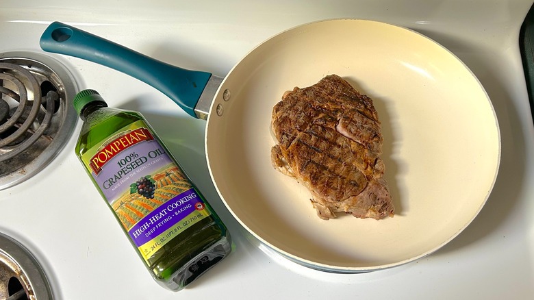 Ribeye steak in a skillet on the stovetop and a bottle of grapeseed oil