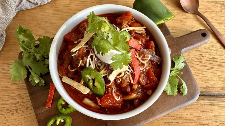 Slow cooker spicy beef chili in a white bowl garnished with fresh cilantro, sour cream, and tortilla strips