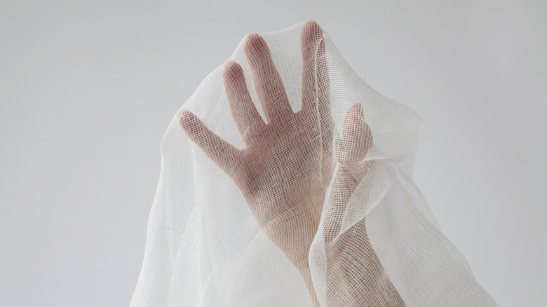 A hand, reaching upward, with cheesecloth draped over it