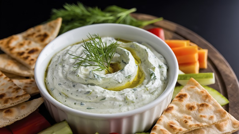 yogurt and dill dip in a ceramic dish with pita and vegetable sticks