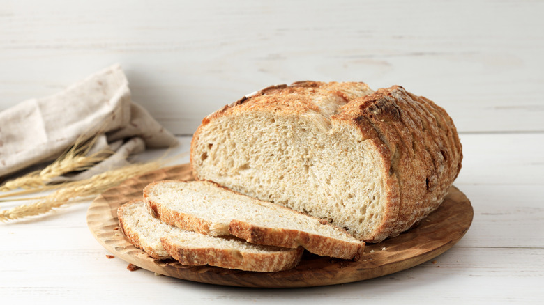 Sliced sourdough bread on a wooden platter against a white wood background