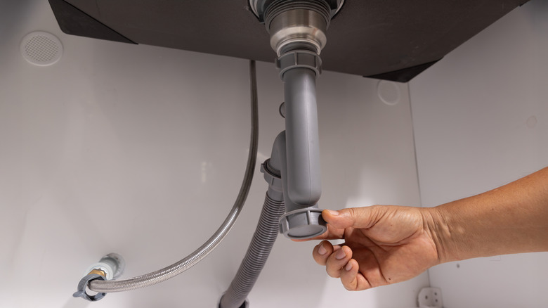 A plumber opening the P-trap under a sink to fix a clogged drain