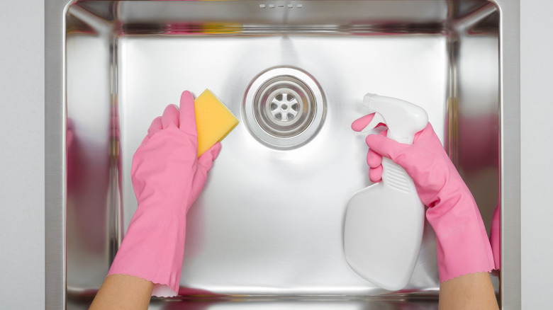 Gloved hands cleaning a stainless steel kitchen sink