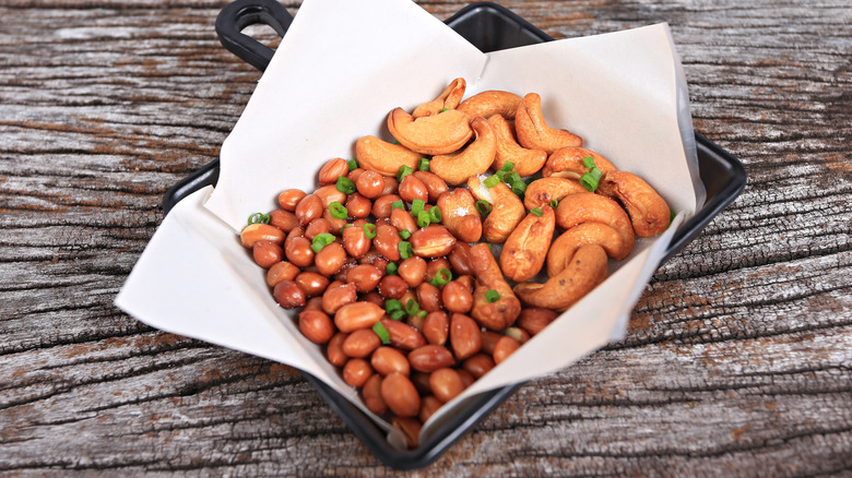 A pan of roasted cashews and seasonings against a wood table.