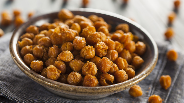 Seasoned roasted chickpeas in a grey stoneware bowl with loose chickpeas spread out on the tabletop around the bowl