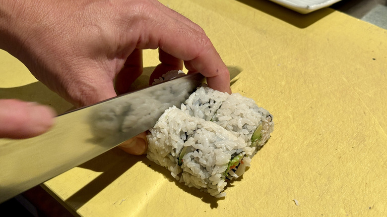 Hands cutting sushi roll with knife